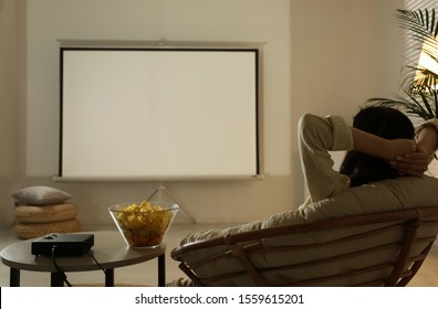 Young Woman Watching Movie Using Video Projector At Home