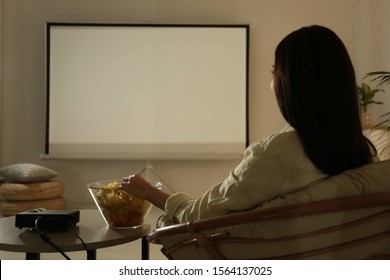 Young Woman Watching Movie Using Video Projector At Home