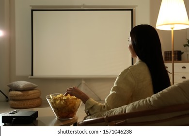 Young Woman Watching Movie Using Video Projector At Home