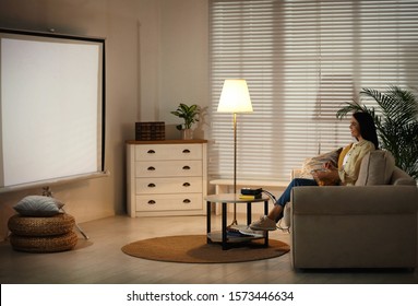 Young Woman Watching Movie Using Video Projector At Home