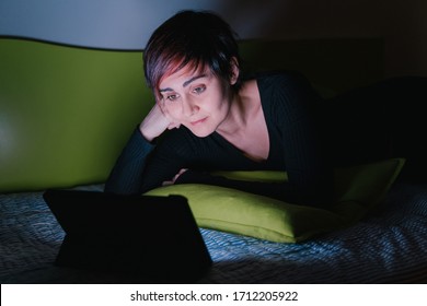 Young Woman Watching Online Tv Show In Bed At Night. People Hooked Up With Entertainment Devices Before Going To Bed. Technology And Leisure Concept. Lifestyle At Home For Young People.