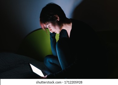 Young Woman Watching Online Tv Show In Bed At Night. People Hooked Up With Entertainment Devices Before Going To Bed. Technology And Leisure Concept. Lifestyle At Home For Young People.