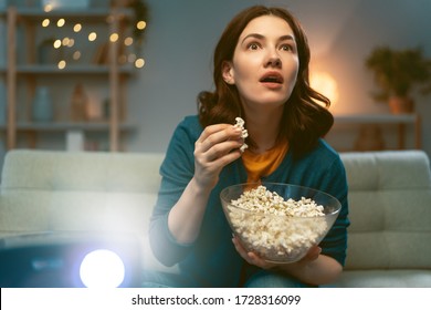 Young woman watching projector, TV, movies with popcorn in the evening. Girl spending time at home. - Shutterstock ID 1728316099