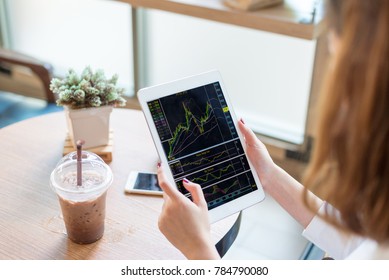 A Young Woman Is Watching A Stock Chart In An IPad At A Coffee Shop.