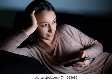 Young woman watching television alone at night on the couch