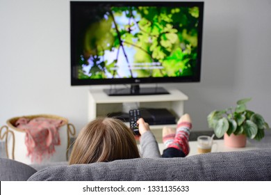 Young woman watching television and subtitles while sitting comfortably sofa at home in living room  Nature  green  documentary  tv screen