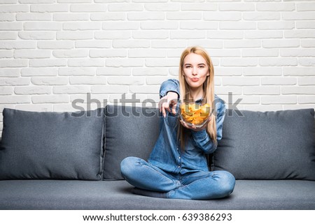 Young woman watching TV on the couch at home and eat chips