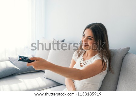 Young woman watching TV in the room. Happy young woman watching tv on sofa.  Woman relax on bed and watching television. Switching tv channels