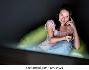 Young Woman Watching TV Sitting On The Beanbag At Home