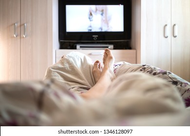 young woman watching TV while lying in bed, only legs are visible, pandemic isolation