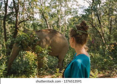 A Young Woman Watching Wild Elephant Eating And Playing In North Thailand In The Middle Of The Jungle. Standing And Enjoying The Freedom In Elephant Sanctuary.