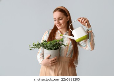 Young woman with watering can and green houseplant on grey background - Powered by Shutterstock