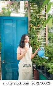 Young Woman Watering Plants On Her City Balcony Garden