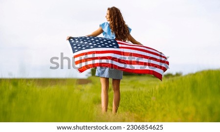 Young woman waves an american flag on blooming meadow. 4th of July. Independence Day. Patriotic holiday. 