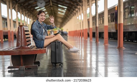 Young Woman Waving Hand While Sitting At Railroad Station Platform
