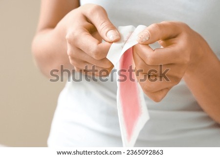 Young woman with wax strip on beige background, closeup