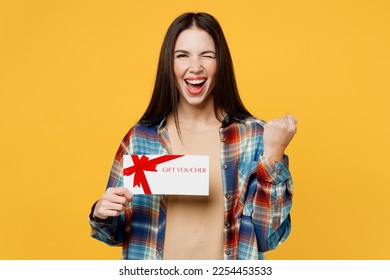 Young woman wear blue shirt beige t-shirt hold store gift certificate coupon voucher card do winner gesture wink blink eye isolated on plain yellow background studio portrait. People lifestyle concept - Shutterstock ID 2254453533