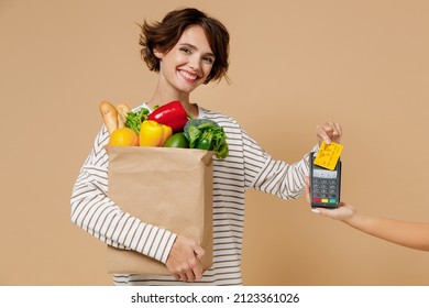 Young woman wear casual clothes hold paper bag with vegetables hold wireless bank payment terminal to process acquire credit card payments isolated on plain pastel beige background Shopping concept - Shutterstock ID 2123361026
