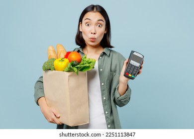 Young woman wear casual clothes holding brown paper bag with food products bank payment terminal process acquire credit card isolated on plain blue background studio portrait. Shop service delivery - Shutterstock ID 2251113847