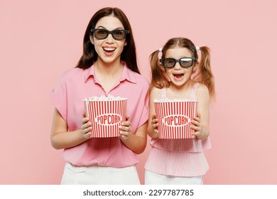 Young woman wear casual clothes with child kid girl 6-7 years old in 3d glasses watch movie film hold bucket of popcorn in cinema. Mother daughter isolated on plain pink background. Family day concept - Powered by Shutterstock