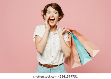 Young woman wear casual clothes hold shopping paper package bags scream sharing hot news about sales discount with hands near mouth isolated on plain pink background. Black Friday sale buy day concept