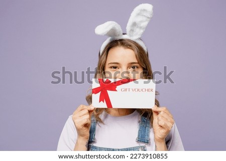 Young woman wear casual clothes bunny rabbit ears hold wicker basket colorful eggs cover mouth with gift coupon voucher card for store isolated on plain pastel purple background. Happy Easter concept