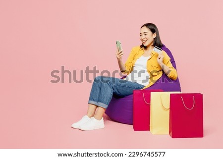 Young woman wear casual clothes sit in bag chair use mobile cell phone credit bank card shopping online order delivery paper package bags isolated on plain pink background. Black Friday sale concept