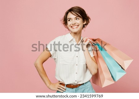 Young woman wear casual clothes hold shopping paper package bags look aside ona rea stand akimbo, arm on waist isolated on plain light pink color background studio. Black Friday sale buy day concept