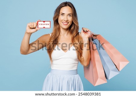 Young woman wear casual clothes hold in hand paper package bags after shopping, show gift certificate coupon voucher card for store isolated on plain blue background. Black Friday sale buy day concept