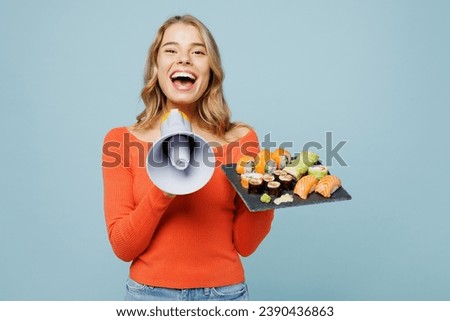 Young woman wear orange casual clothes scream in megaphone announces discounts sale Hurry up hold eat raw fresh sushi roll served on black plate Japanese food isolated on plain blue background studio