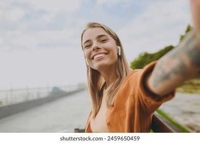 Young woman wear orange shirt casual clothes listen music in earphones do selfie shot on mobile cell phone sit on bench walk rest relax in spring city park outdoors on nature. Urban lifestyle concept - Powered by Shutterstock