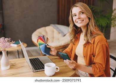 Young IT woman wear orange shirt use laptop pc computer hold color palette mobile cell phone sit alone at table in coffee shop cafe restaurant indoors work or study Freelance office business concept - Powered by Shutterstock