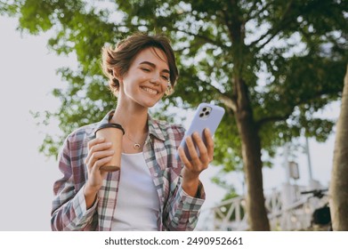 Young woman wear shirt casual clothes hold use mobile cell phone drinking coffee sits walk rest relax in spring sunshine green city park near sea outdoors on nature. Urban lifestyle leisure concept - Powered by Shutterstock