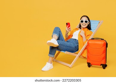 Young woman wear summer clothes sit in deckchair use show mobile cell phone isolated on plain yellow background. Tourist travel abroad in free spare time rest getaway. Air flight trip journey concept - Shutterstock ID 2272203305