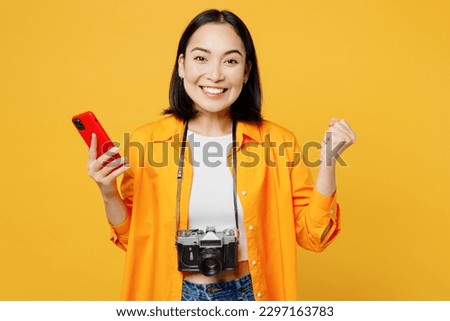 Young woman wear summer clothes hold use mobile cell phone do winer gesture isolated on plain yellow background. Tourist travel abroad in free spare time rest getaway. Air flight trip journey concept