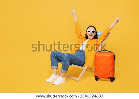 Young woman wear summer clothes sit in deckchair spread hands show v-sign isolated on plain yellow background. Tourist travel abroad in free spare time rest getaway. Air flight trip journey concept