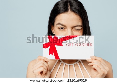 Young woman wear swimsuit hold cover eye with store gift certificate coupon voucher card wink near hotel pool isolated on plain pastel light blue background. Summer vacation sea rest sun tan concept