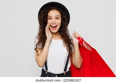 Young woman wear t-shirt hat hold in hand red paper package bags after shopping scream hot news about sales discount isolated on plain solid white color background. Black Friday sale buy day concept