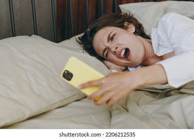 Young woman wear white shirt pajama she lying in bed hold mobile cell phone alarm yawning rest relax spend time in bedroom lounge home in own room hotel wake up in early morning Real estate concept - Shutterstock ID 2206212535