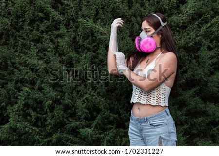 young woman wearing antibacterial mask and latex gloves outdoors as disease prevention and covid-19 and adjusting protective gloves