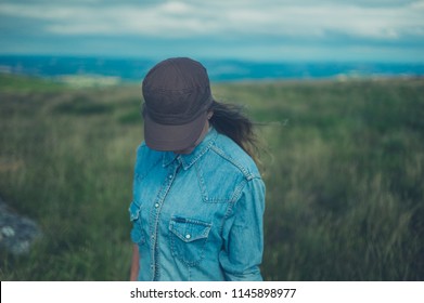 A Young Woman Wearing A Baseball Cap Is Standing On A Hilltop