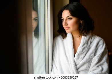 Young Woman Wearing A Bathrobe And Looking Outside A Window In His Hotel Room