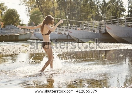 Young woman wearing a bikini splashing and playing in river