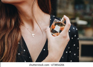 young woman wearing black and white polka dot dress posing with a bottle of expensive perfume. beautiful and stylish european fashion blogger posing with perfume outdoors. perfect summer outfit. 