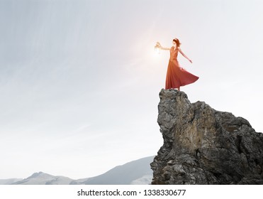 Young woman wearing blindfold with lantern standing on rock top - Shutterstock ID 1338330677