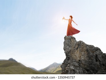Young woman wearing blindfold with lantern standing on rock top - Shutterstock ID 1350945737