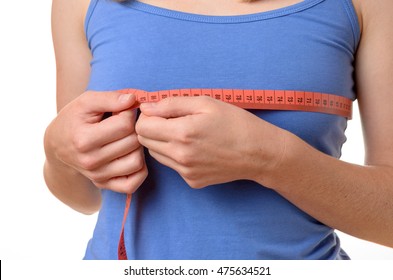 Young woman wearing a blue summer t-shirt measuring her breasts with a tape measure, close up torso view on white