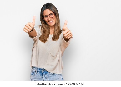 Young woman wearing casual clothes and glasses approving doing positive gesture with hand, thumbs up smiling and happy for success. winner gesture.  - Powered by Shutterstock