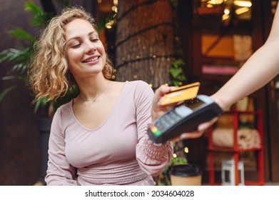 Young woman wearing casual clothes at cafe buy breakfast sit at table hold wireless modern bank payment terminal to process acquire credit card payments relax in restaurant during free time indoors.