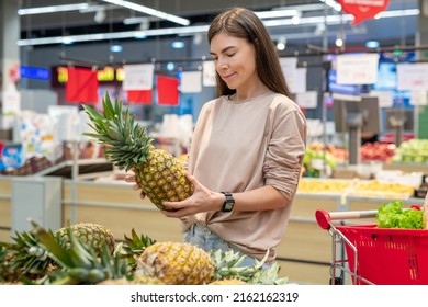 Young Woman Wearing Casual Outfit Choosing Best Pinapple In Modern Supermarket, Copy Space